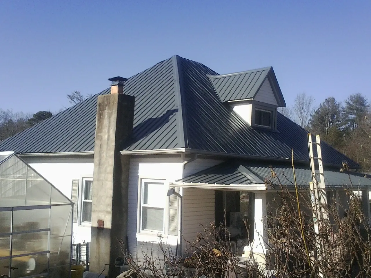 Dark blue standing seam metal roof on a white farmhouse with dormer — Slate & Tile Roof Repair by Roofing Brothers in Henrieville