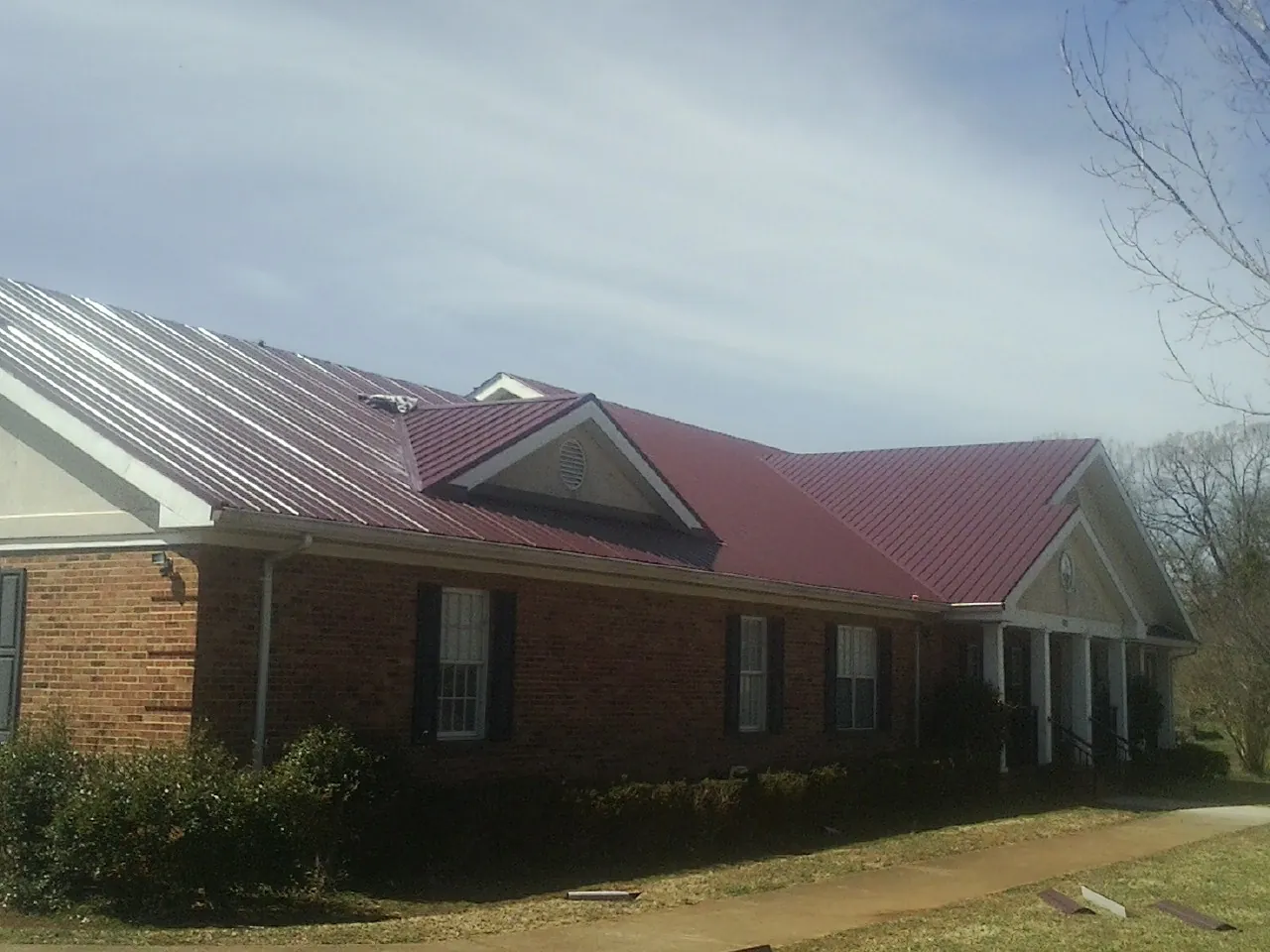 Red metal roof with gabled entries on a long brick building, from a Hail Damage Roof Repair job in Henrieville