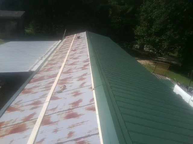 Old rusted panels beside newly installed green metal roofing — Wind Damage Roof Repair by Roofing Brothers in Henrieville