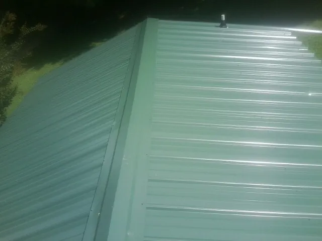 New green metal panels meeting at the ridge of a roof — Flat Roof Repair work by our crew in Henrieville