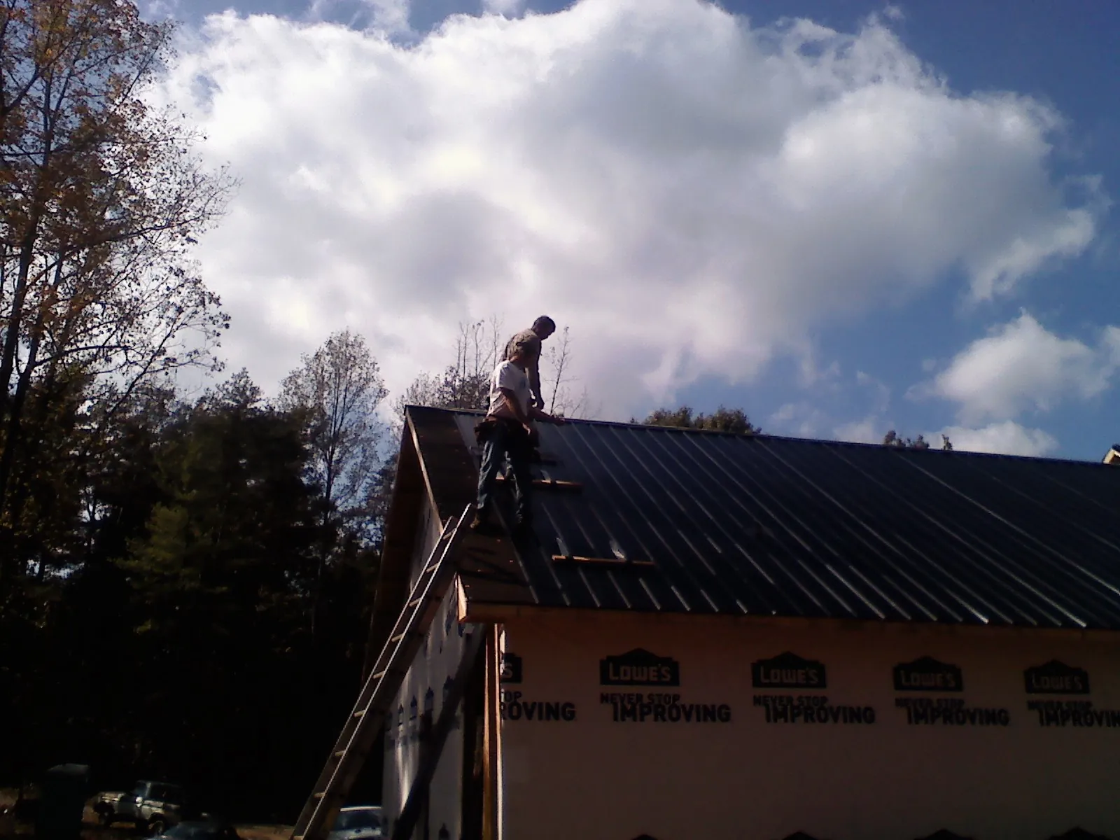 Roofer fastening dark metal panels high against a cloudy sky, from a Roof Inspection job in Henrieville