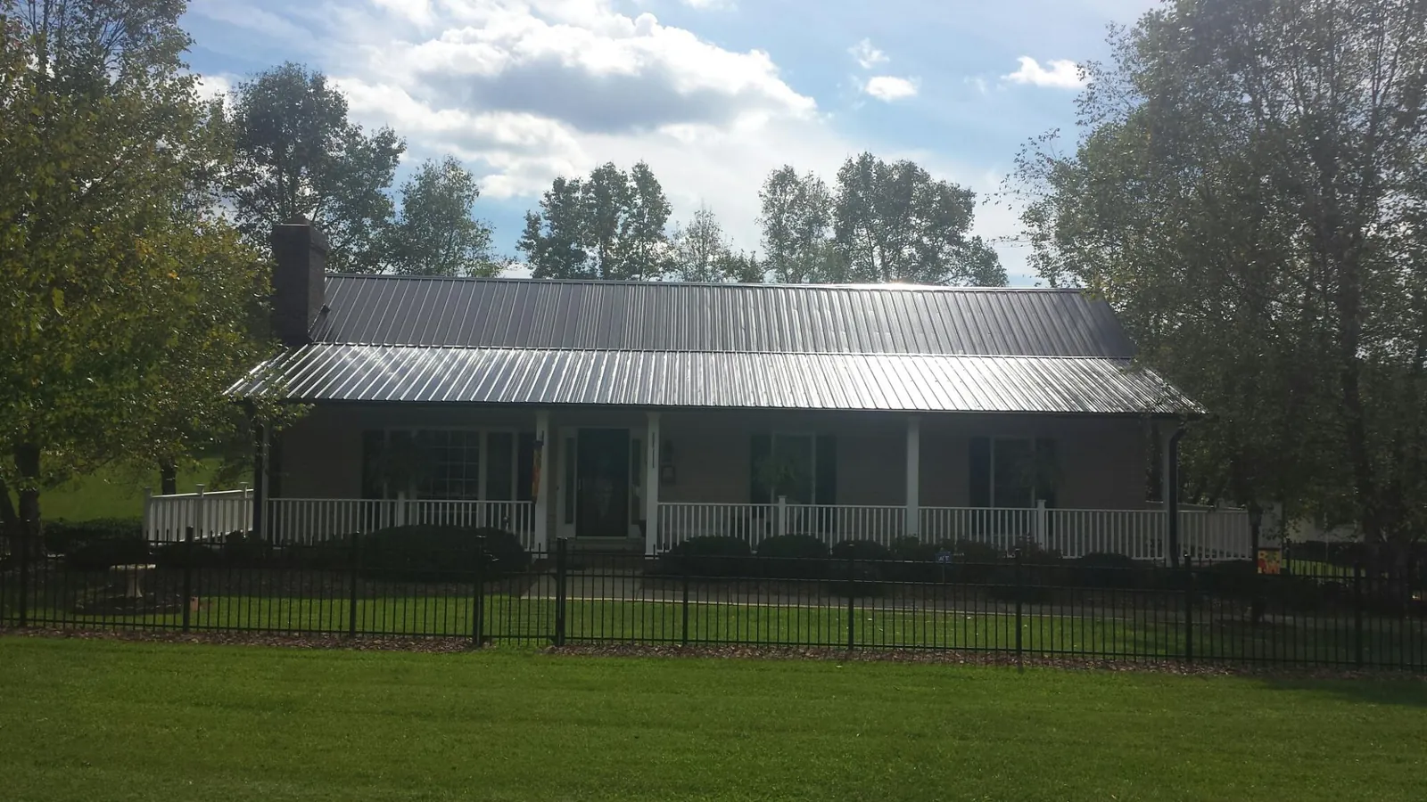 Gray metal roof on a brick ranch with a full width front porch — Gutter Guard Installation work by our crew in Henrieville